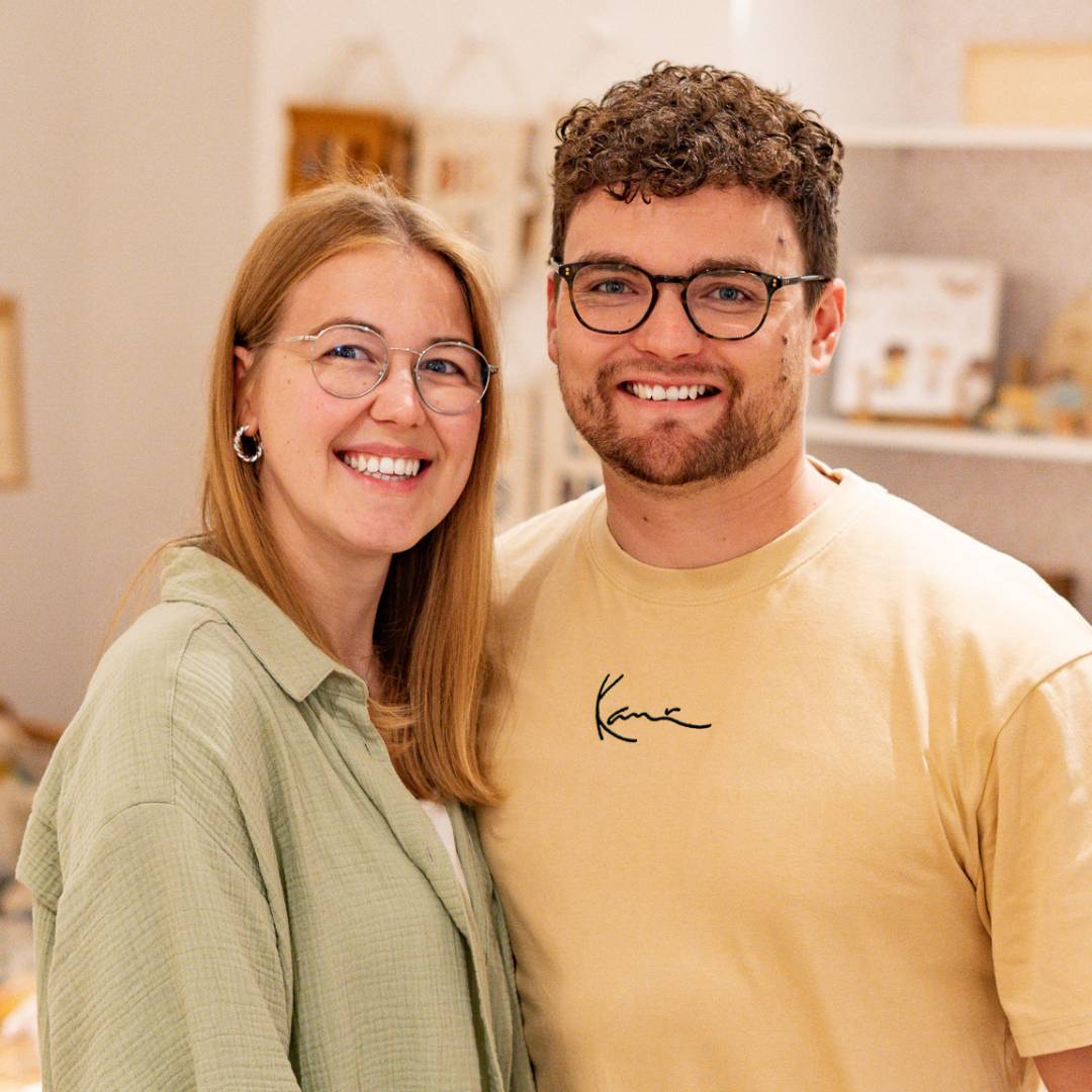 Lena und Stefan nebeneinander, die lächelnd im Store in Steinfeld stehen und in die Kamera schauen.